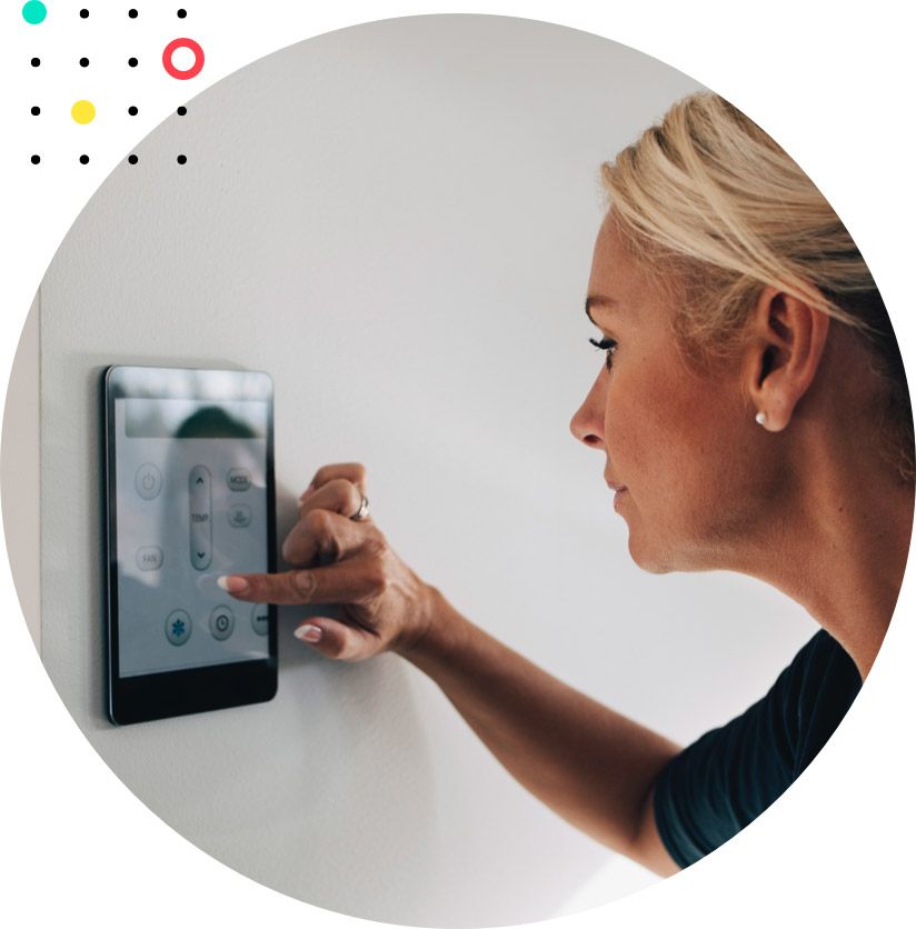 Image of a woman inside her house, using a smart touchscreen to change her thermostat settings.